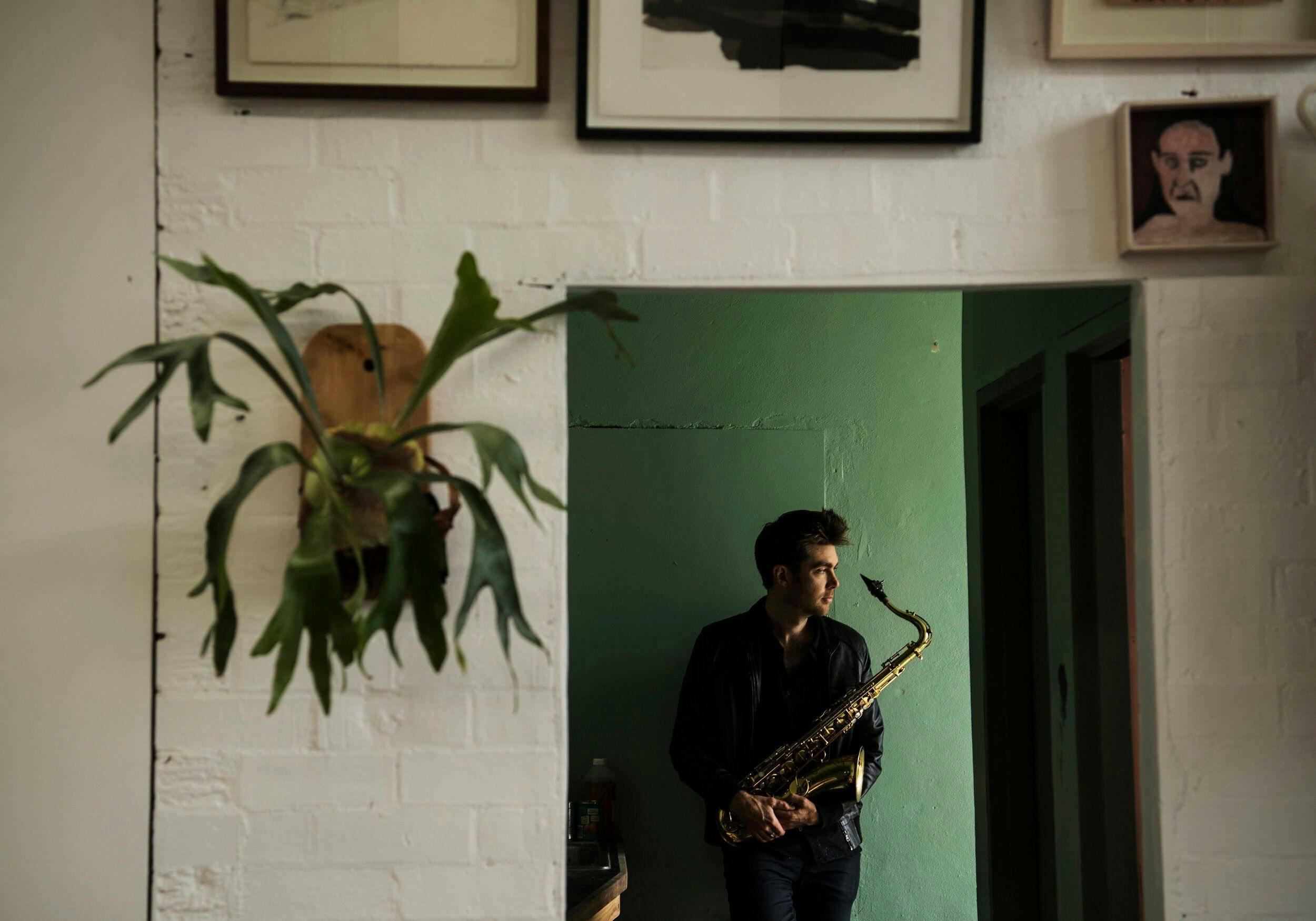 A man playing saxophone in a room with pictures on the wall.