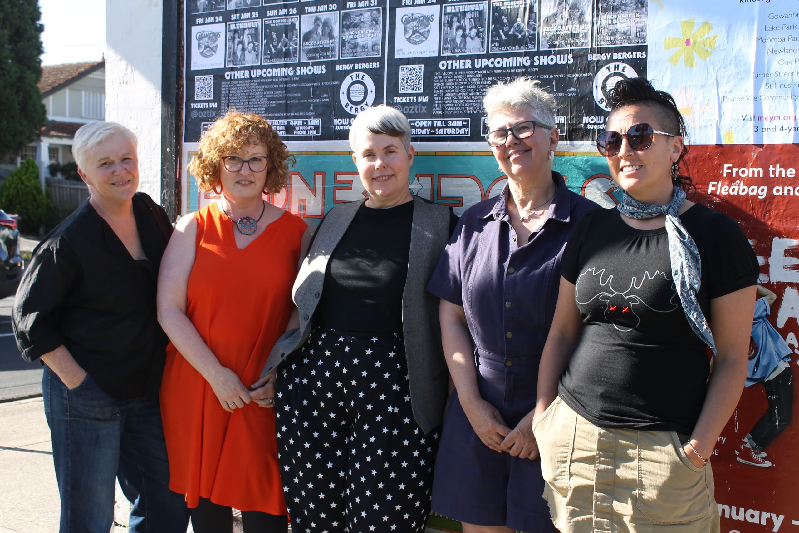 a group of women standing in front of a wall covered in street posters