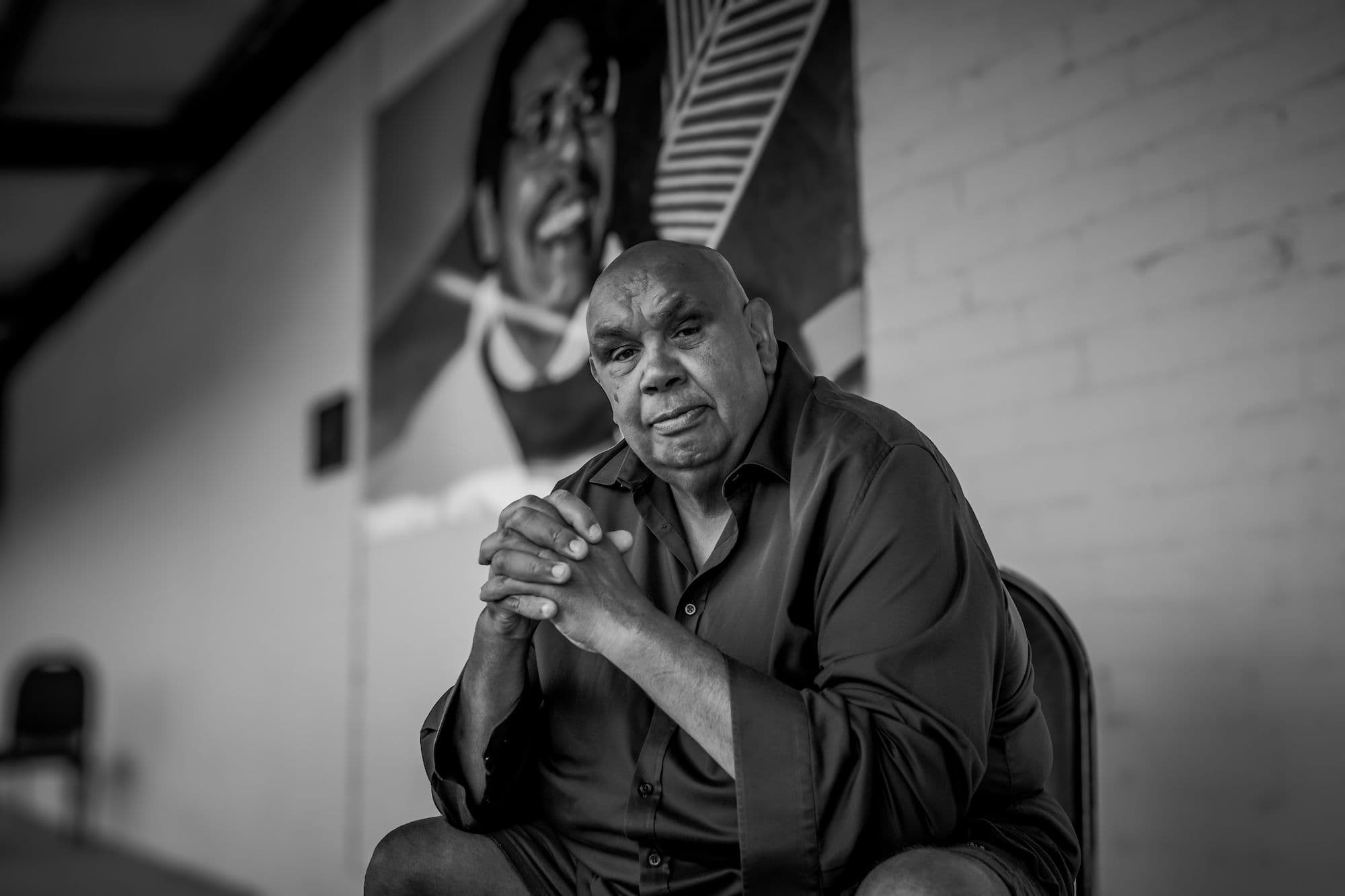A black and white photo of an older man sitting thoughtfully on a chair, exuding wisdom and experience.