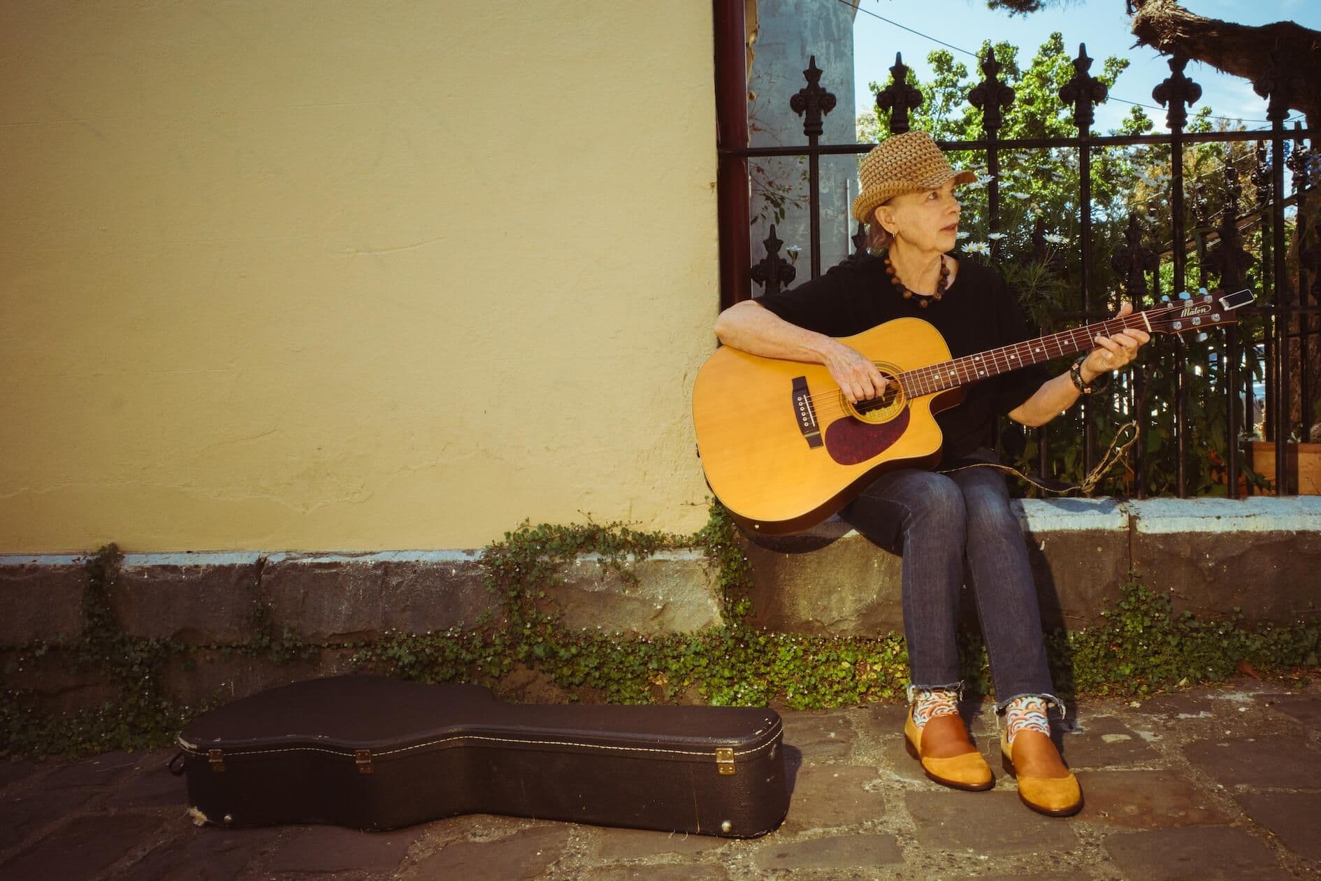 A woman sitting in front on a fence playing acoustic guitar.
