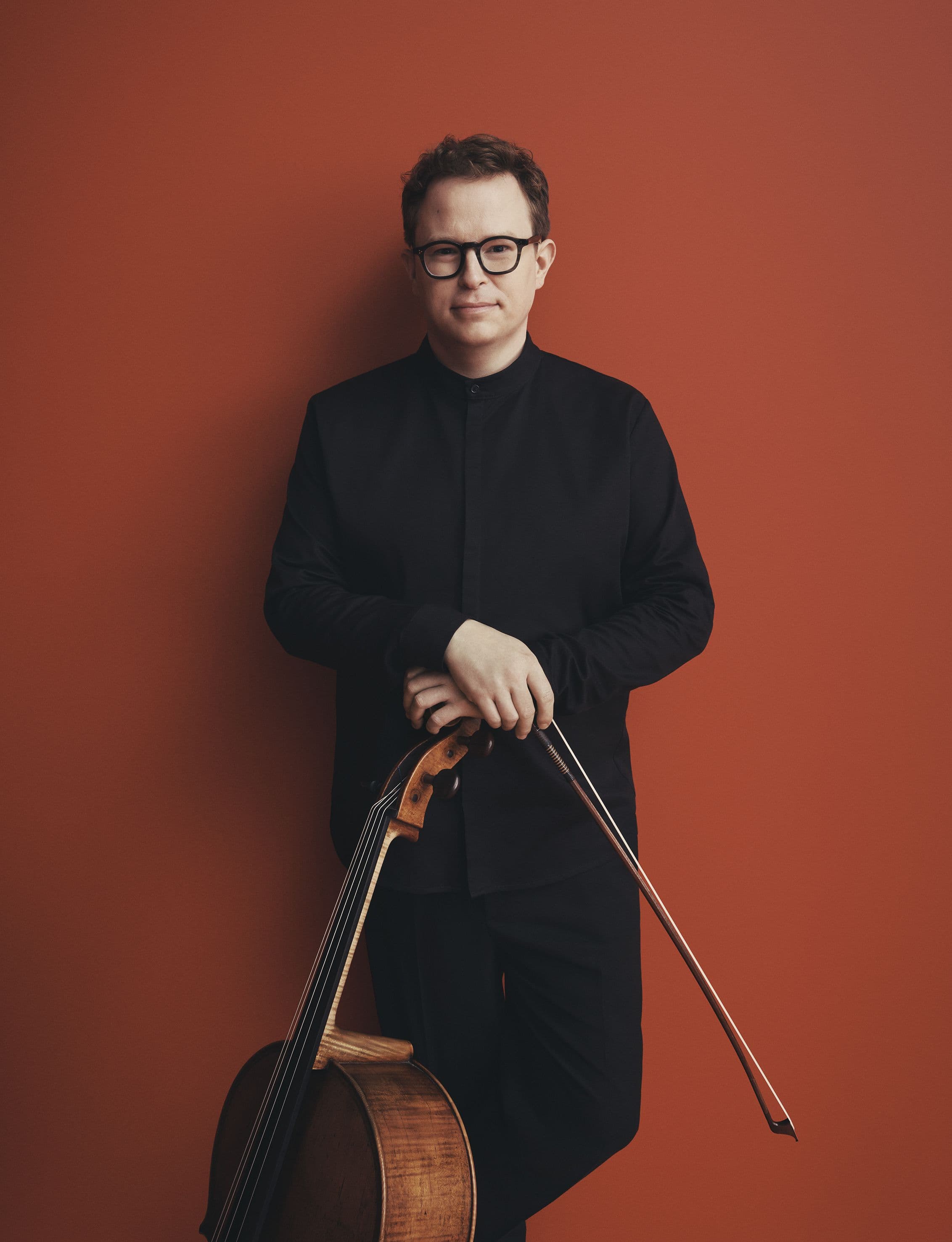A man standing against the wall holding a cello