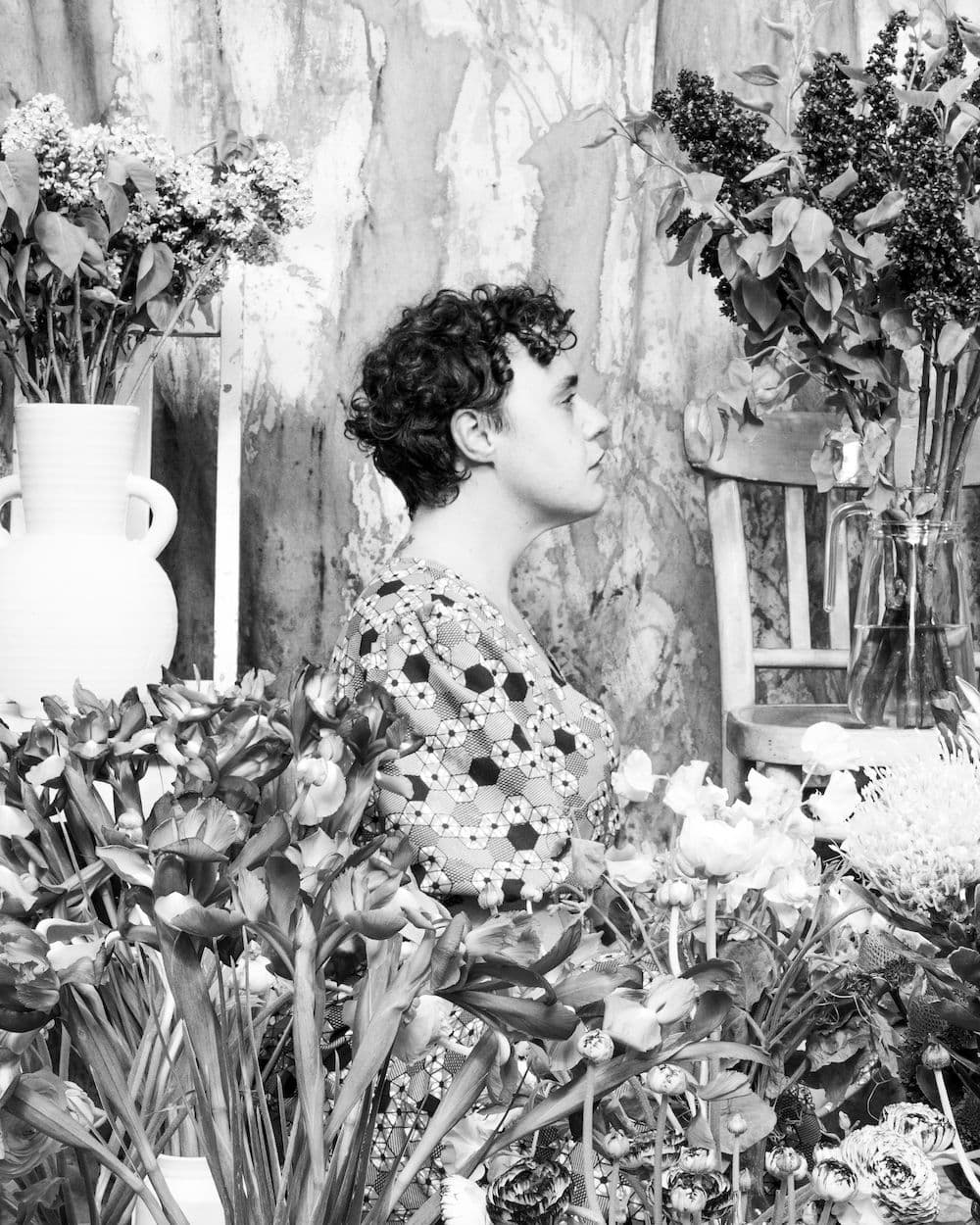 a black and white image of a person facing the side and mostly hidden by indoor plants