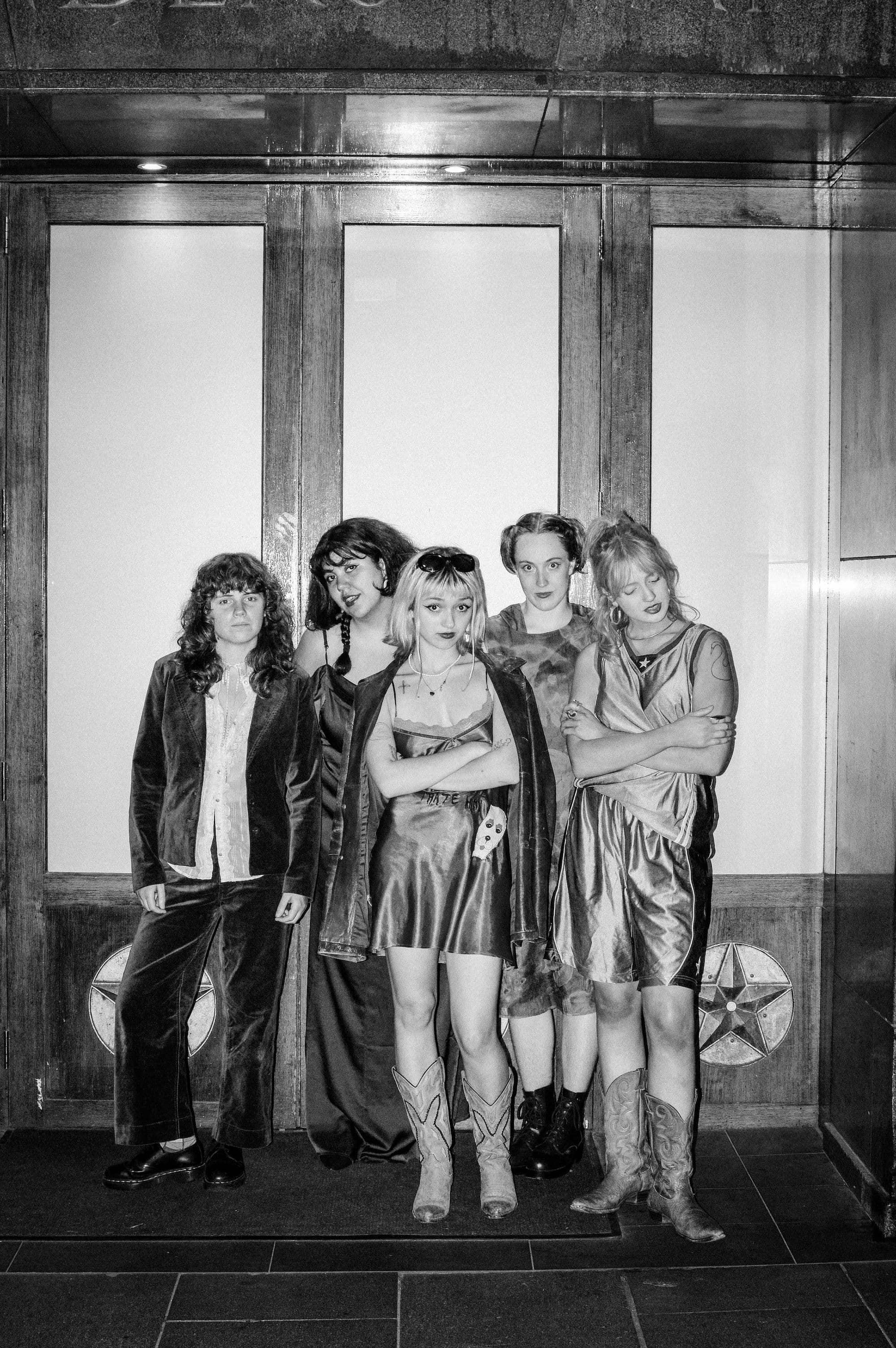 A bunch of friends standing together, waiting for the elevator to open, with smiles and casual conversation.